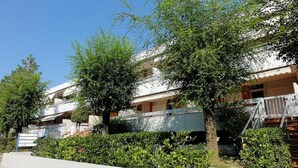 Un immeuble résidentiel doté de nombreux balcons, d’une façade blanche et entouré de verdure.