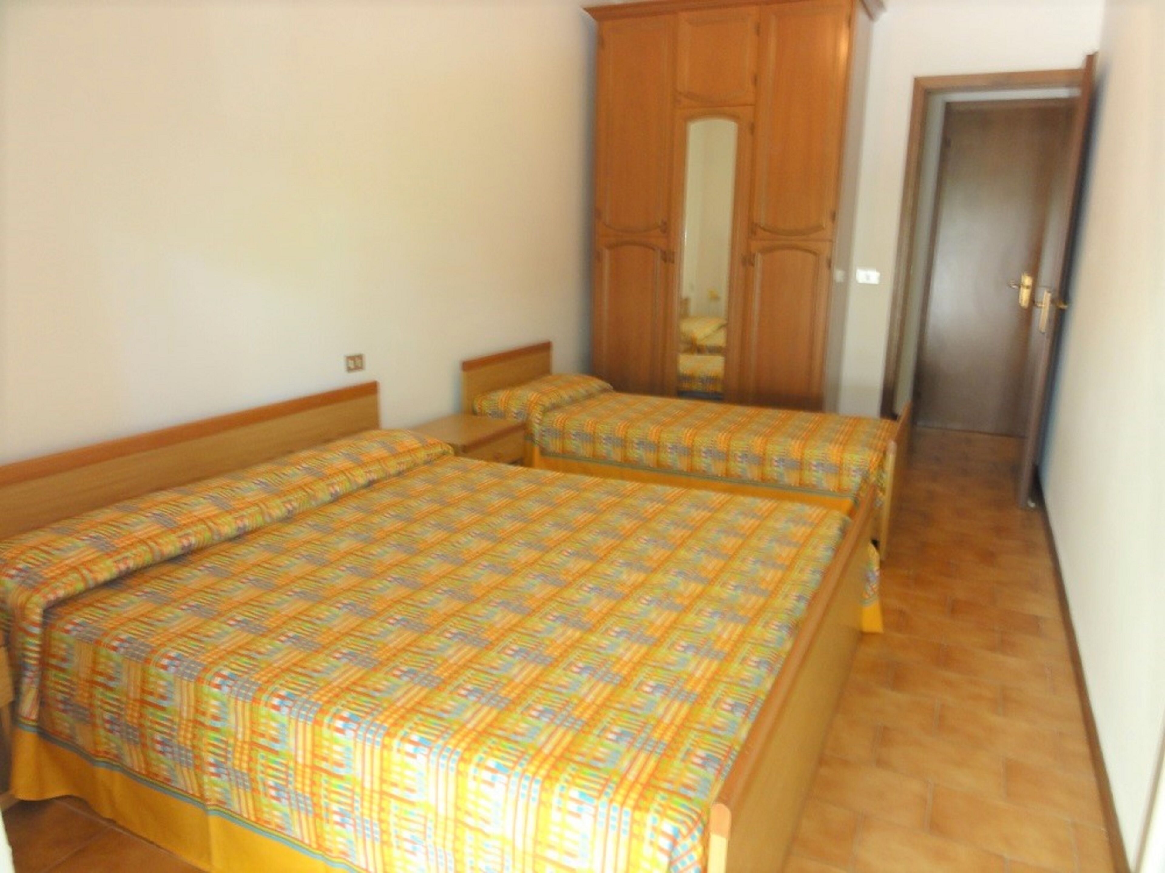 Ein Schlafzimmer mit zwei Einzelbetten, Holz-Kopfteilen, einem Kleiderschrank und einer Tür zu einem weiteren Raum.