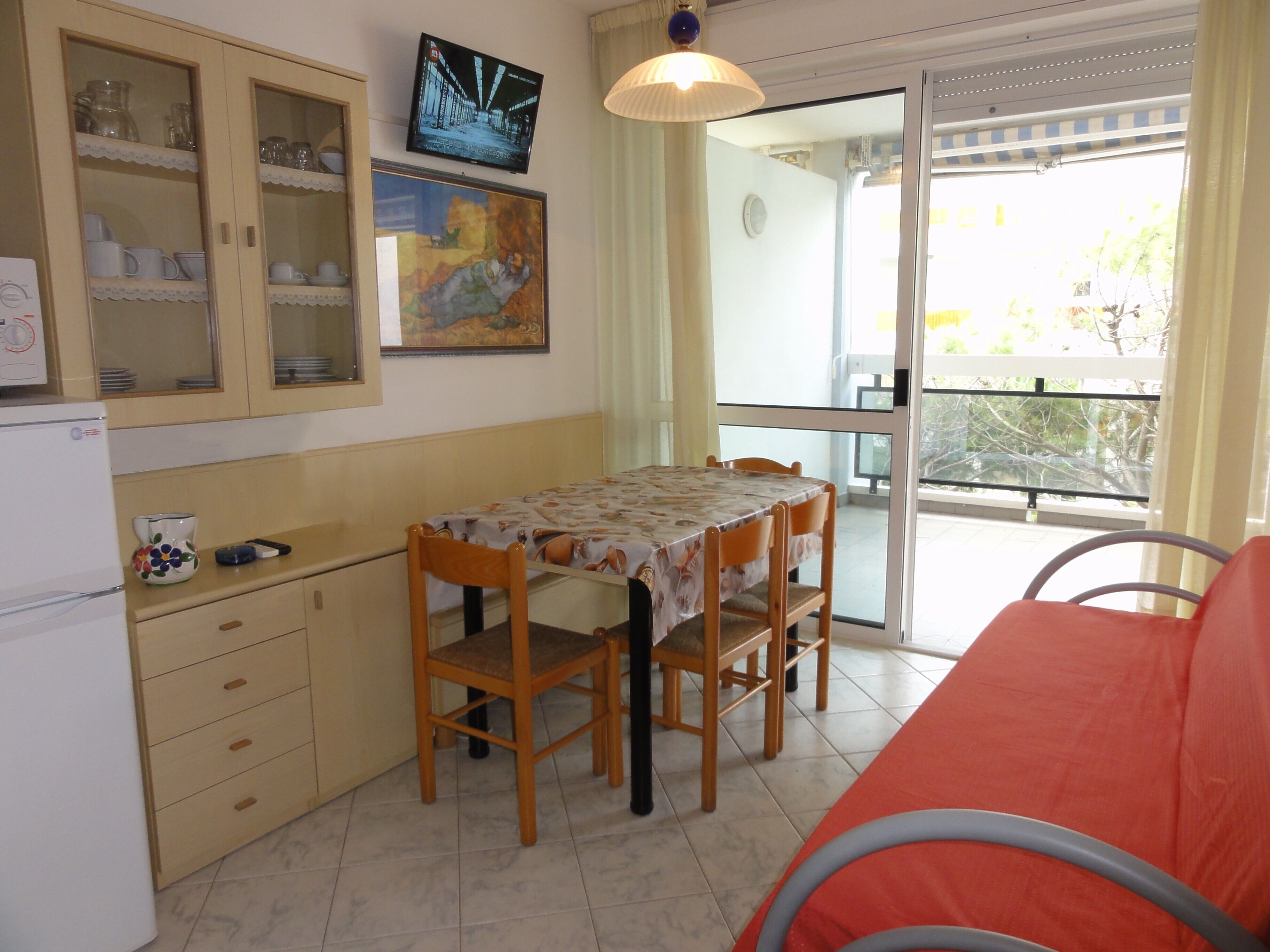Une petite cuisine avec une table et des chaises, un réfrigérateur et un téléviseur fixé au mur.
