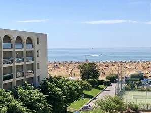 A multi-story building with a parking garage, a beach with umbrellas, and a clear view of the sea. - Condominio Aurora (San Michele al Tagliamento)