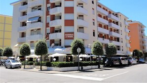 A multi-story building with balconies, a cafe on the ground floor, and a sign reading "AUSONIA al MARE GELAT." - Condominio Ausonia Al Mare (San Michele al Tagliamento)