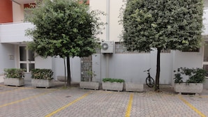 A parking area with hexagonal paving and yellow lines, surrounded by planters with various shrubs and a bicycle leaning against a wall. - Condominio Ausonia Al Mare (San Michele al Tagliamento)