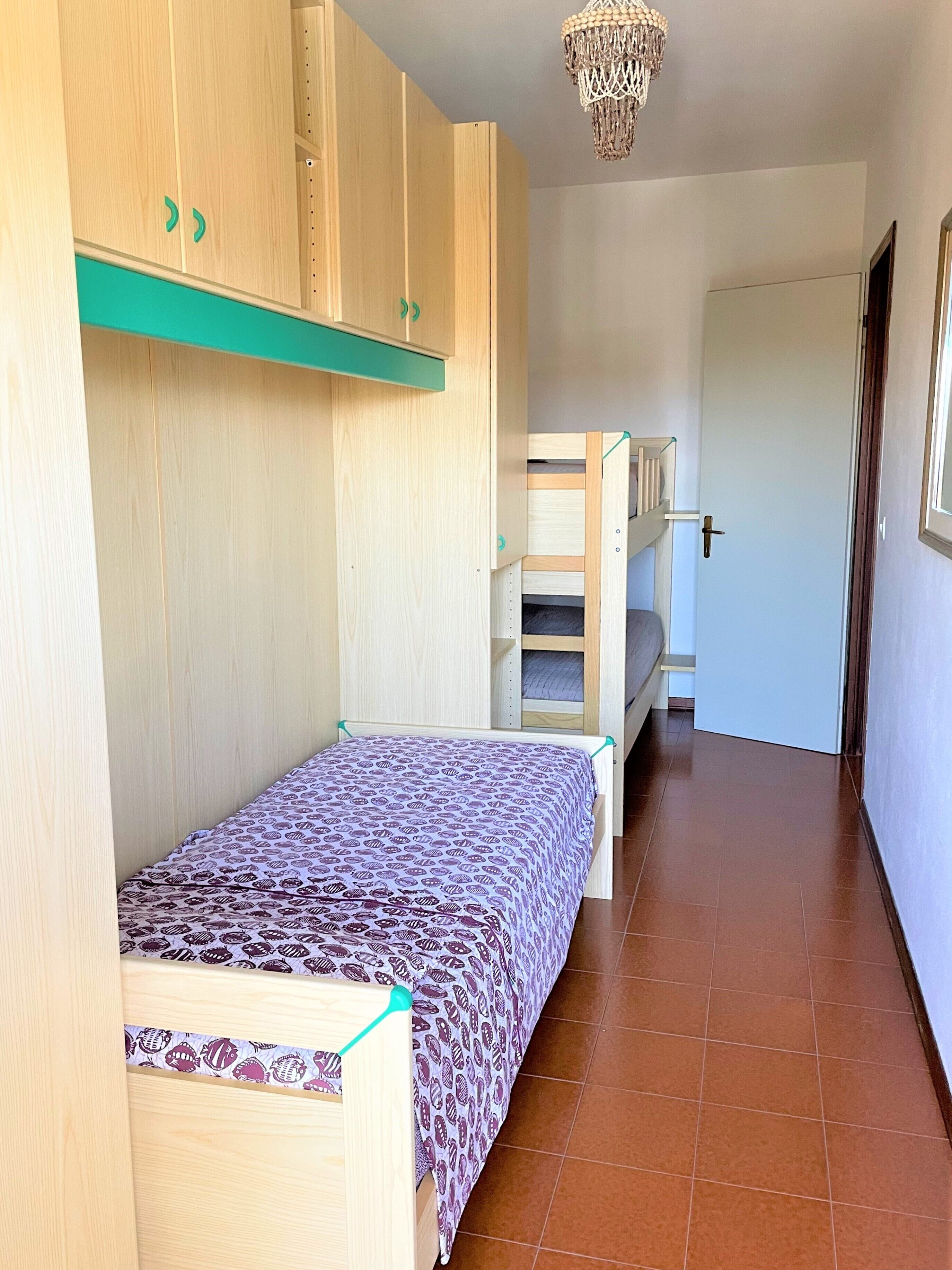 A bedroom with a bunk bed, a single bed, wooden cabinets, and a chandelier.