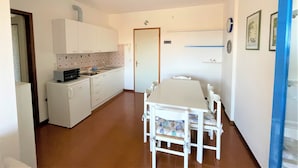 A compact kitchen with white cabinets, a sink, and a microwave. There is a dining table with chairs in the center of the room. - Condominio Biloba (San Michele al Tagliamento)