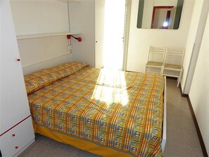 Une petite pièce lumineuse, avec un lit, une chaise et un miroir.