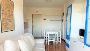 A white sofa, a dining table with chairs, and a TV on a cabinet. - Condominio Biloba (San Michele al Tagliamento)