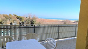 A balcony with a white table and chairs, a metal railing, and a view of the sea and landscape. - Condominio Biloba (San Michele al Tagliamento)