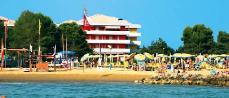 A beach with a multi-story building, umbrellas, and beachgoers.