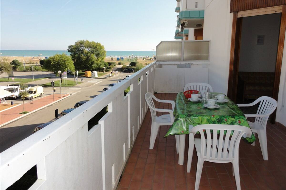 A balcony with a table and chairs, overlooking a street and beach.