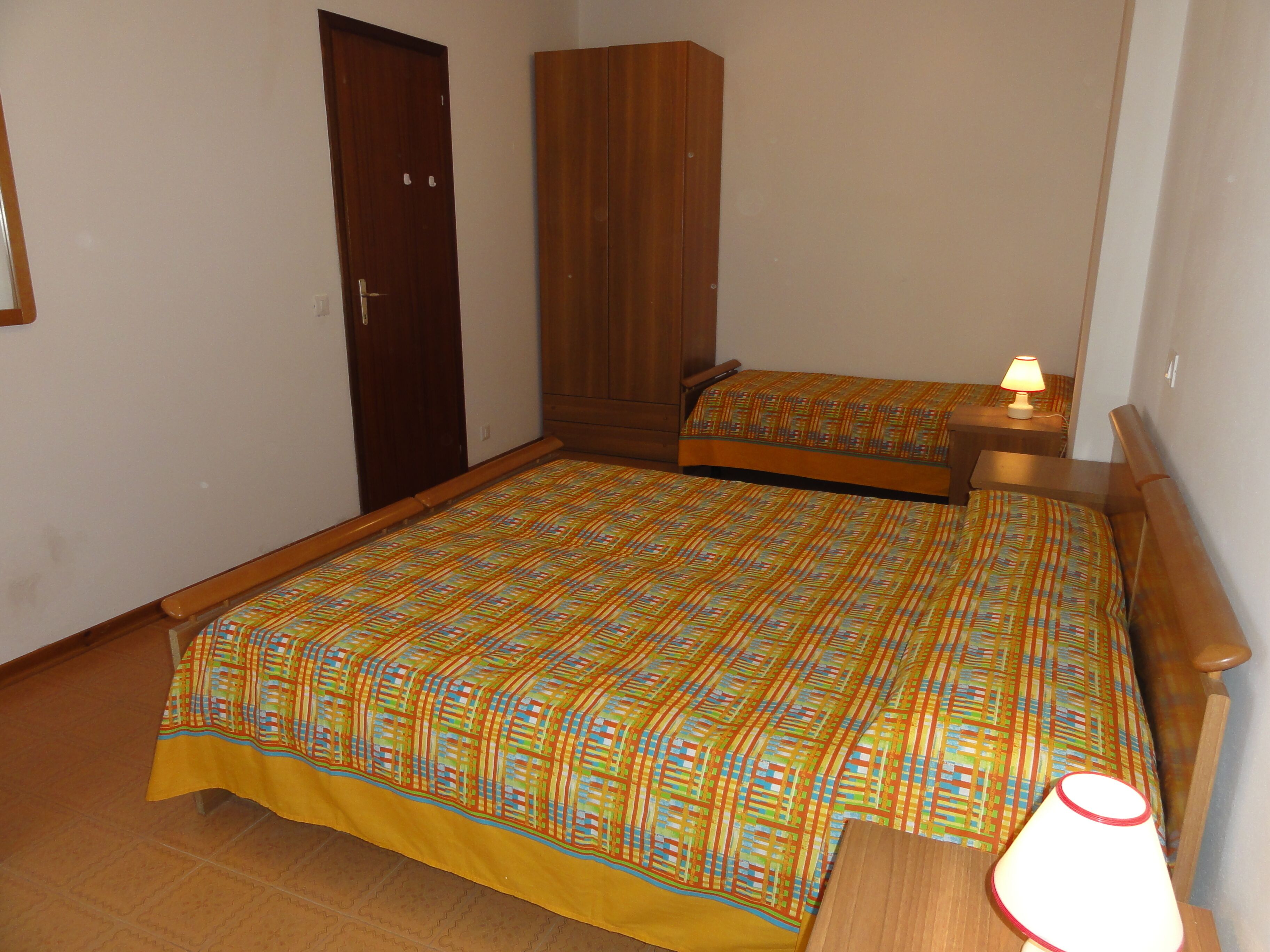 Un dormitorio con dos camas, un armario y una mesita de noche con lámpara.