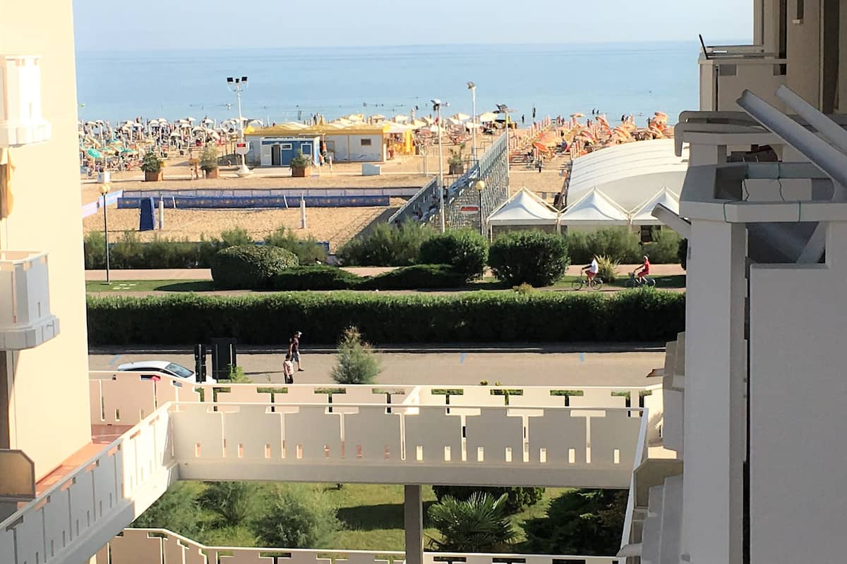 A view of a beach with umbrellas and people, a building with a balcony, and a clear sky.