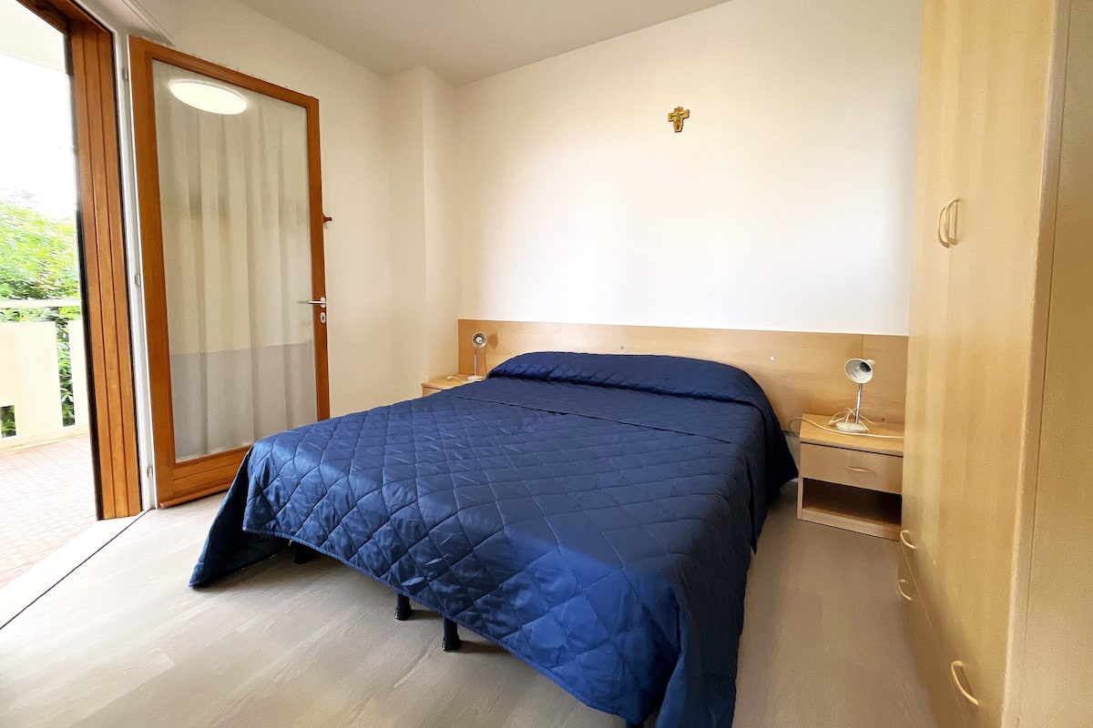 A bedroom with a bed, a nightstand, a mirror, and a door leading to a balcony.
