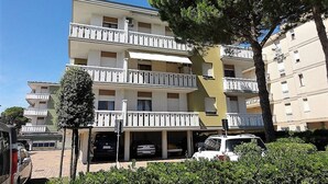 A multi-story residential building with balconies, a parking area, and a tree in the foreground. - Condominio Diana Est (San Michele al Tagliamento)