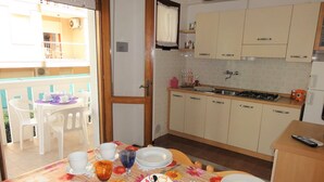 A dining area with a table set for four, a kitchen with beige cabinets, and a balcony with white chairs. - Condominio Diana Est (San Michele al Tagliamento)