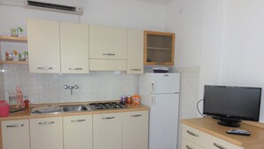 A compact kitchen with white cabinets, a gas stove, a refrigerator, and a television on a wooden counter. - Condominio Diana Est (San Michele al Tagliamento)