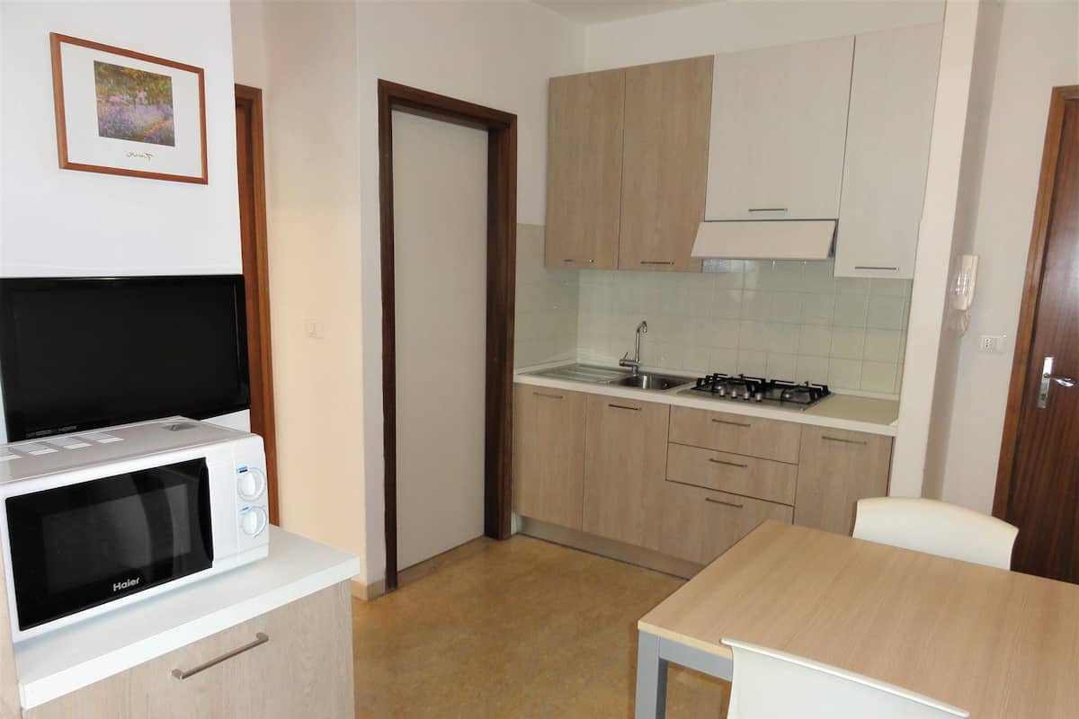 Una cocina compacta con microondas, pileta y cocina. Hay una puerta que da a otra habitación y un cuadro en la pared.