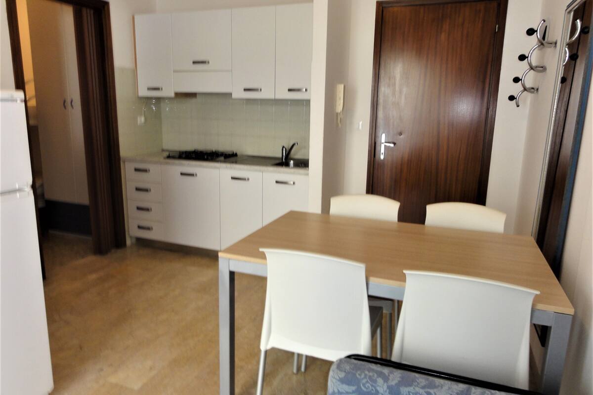 Una cocina compacta con armarios blancos, una puerta de madera y un área de comedor con una mesa y sillas.