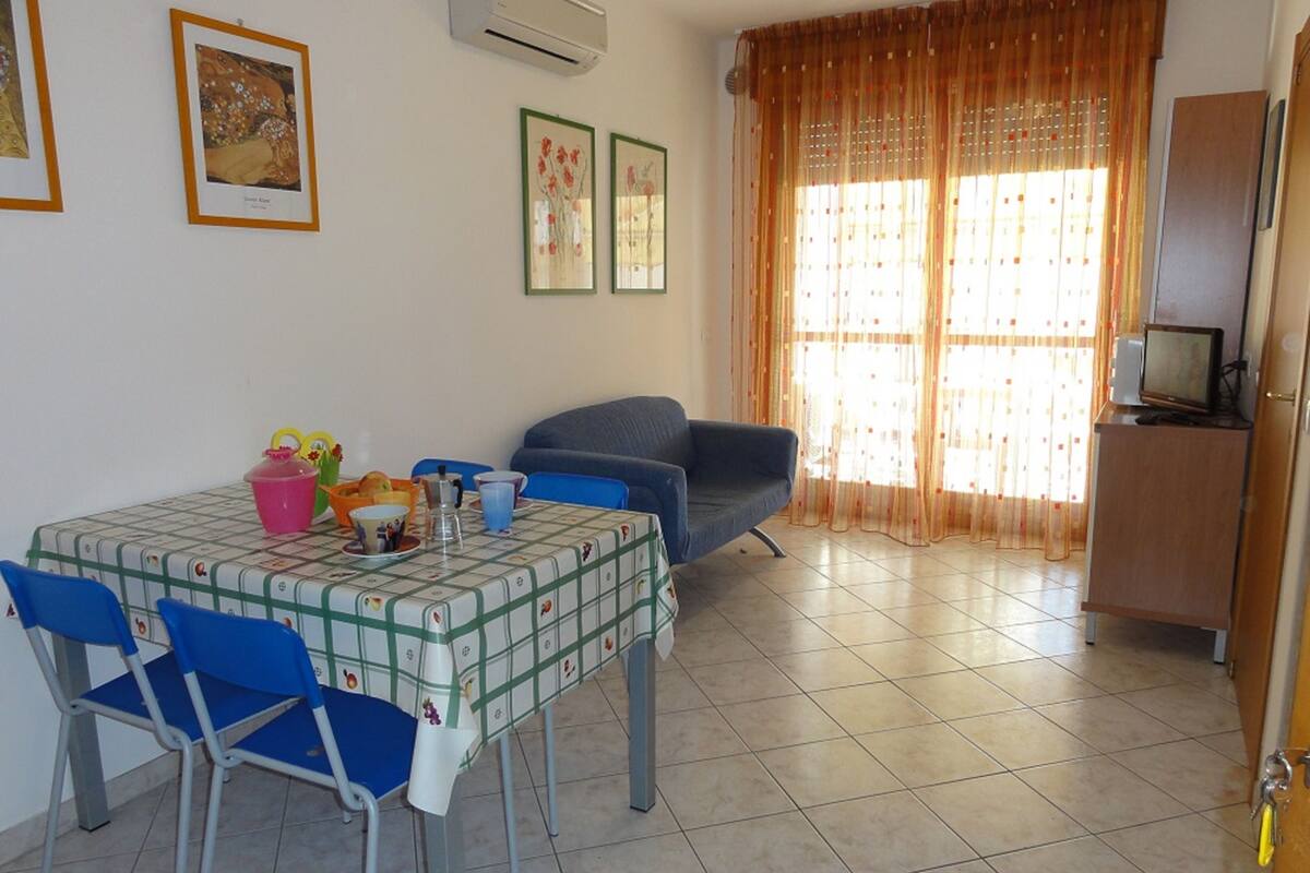 A dining area with a table set for four, blue chairs, a blue sofa, and a television on a cabinet.