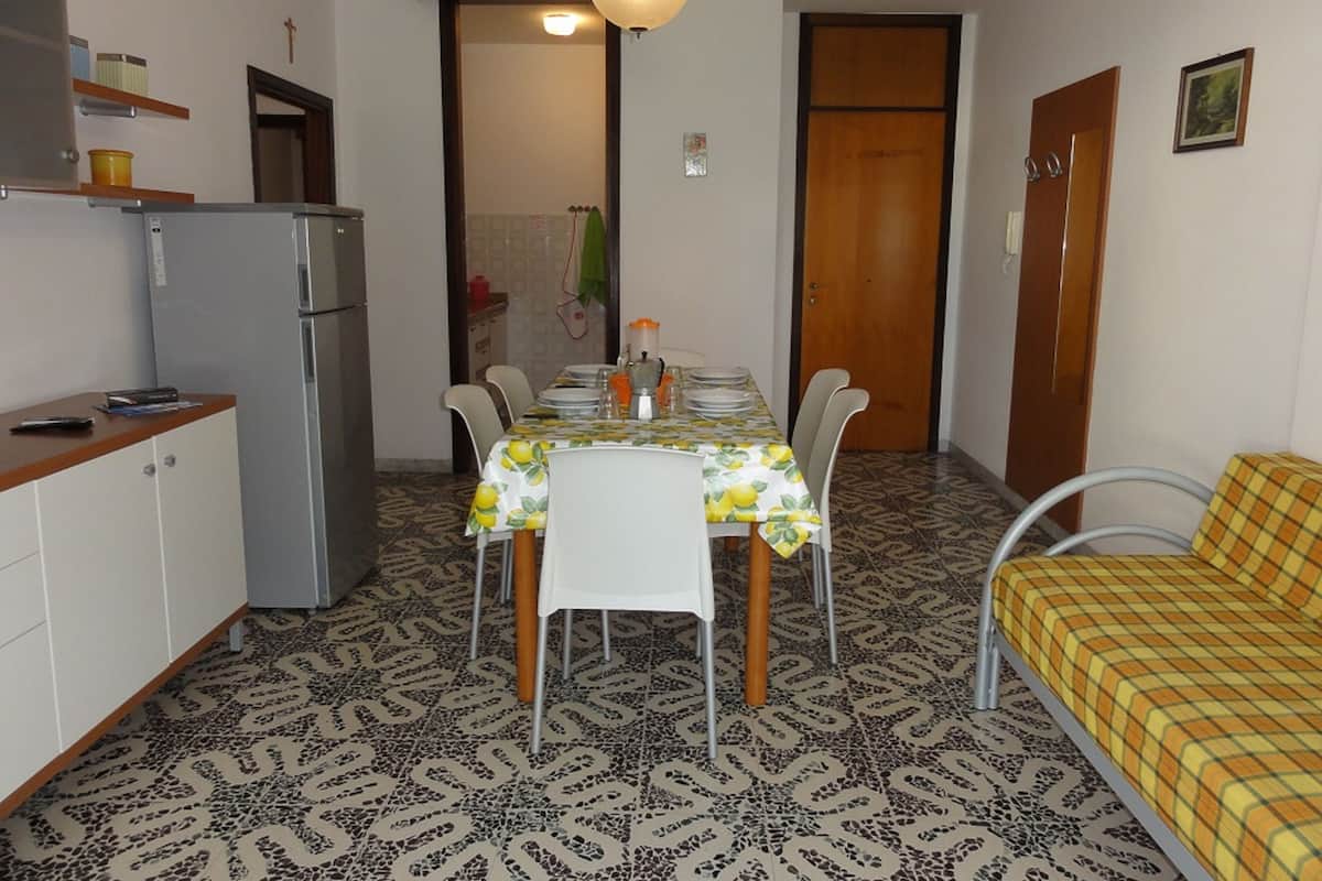 A compact kitchen with a refrigerator, dining table, chairs, and a sofa.