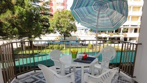 Un balcon avec une table et des chaises, un sol à motifs et une vue sur une piscine et des bâtiments.