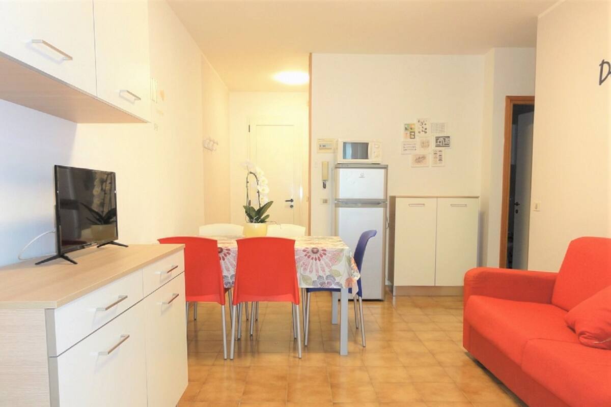 Cocina compacta con mesa, sillas, un sofá rojo y un televisor sobre un mueble.