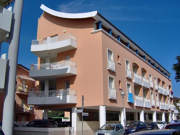 A multi-story building with balconies, a parking area, and a clear blue sky. - Condominio Isolina (San Michele al Tagliamento)
