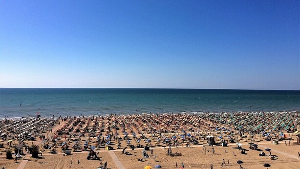 Ein überfüllter Strand mit zahlreichen Sonnenschirmen und Liegestühlen.