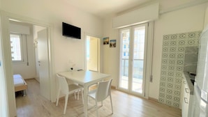 Een kleine keuken met een witte tafel, stoelen en een televisie erboven.