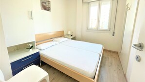 Een slaapkamer met een bed, nachtkastje, lamp en een kleine plant.