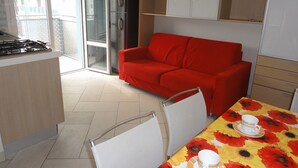 A modern kitchen with a red sofa, dining table with floral tablecloth, and a refrigerator. - Condominio Molent (San Michele al Tagliamento)