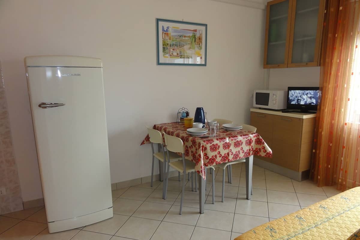 A small, clean room with a dining table, chairs, a refrigerator, a microwave, and a television.