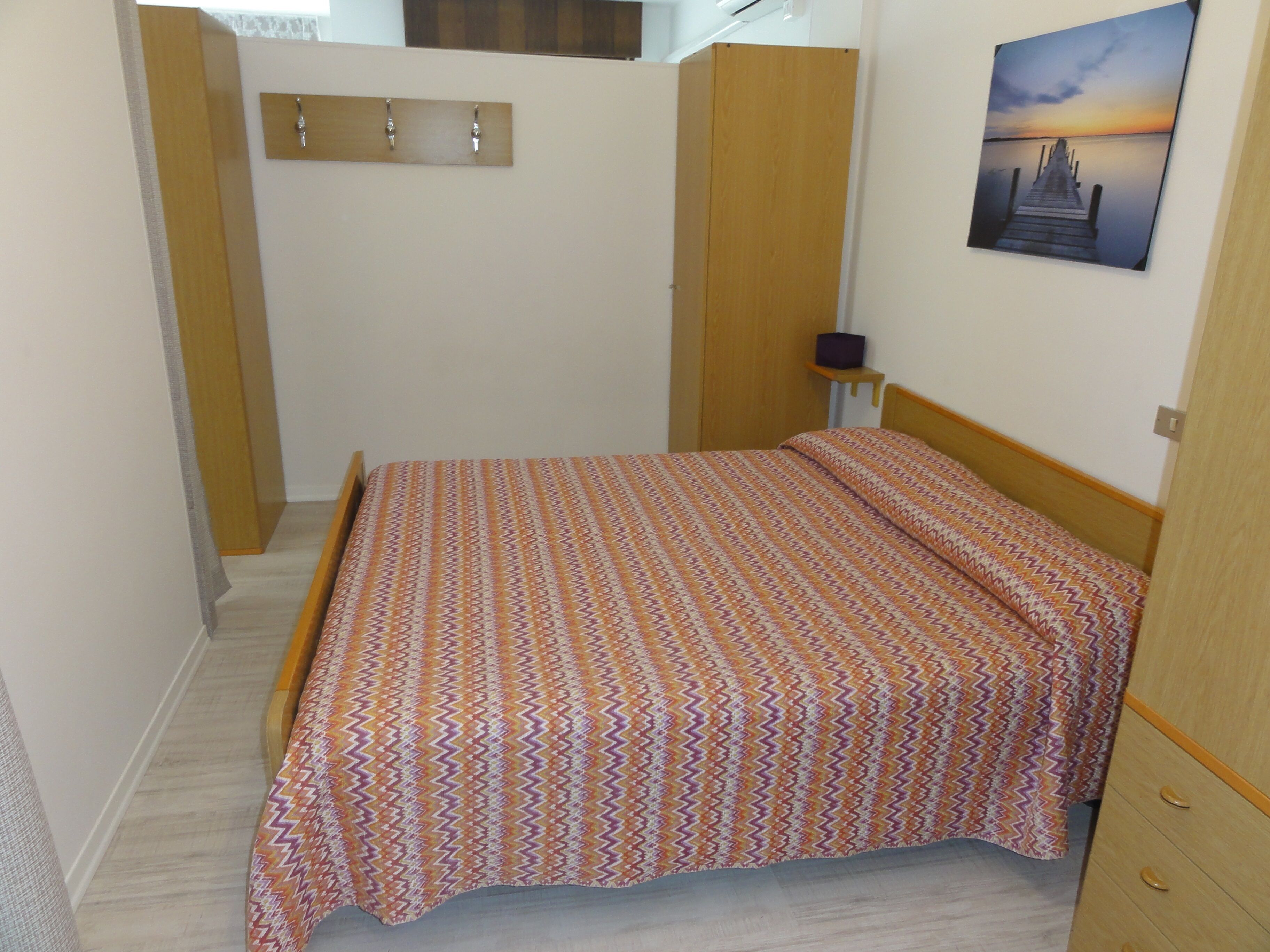 Una camera da letto piccola con un letto, un armadio in legno, un comodino e un quadro appeso al muro.