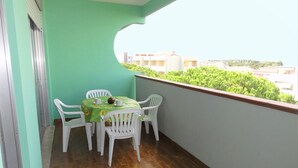 Un balcón con mesa y sillas, un mantel verde y vistas a edificios y vegetación.