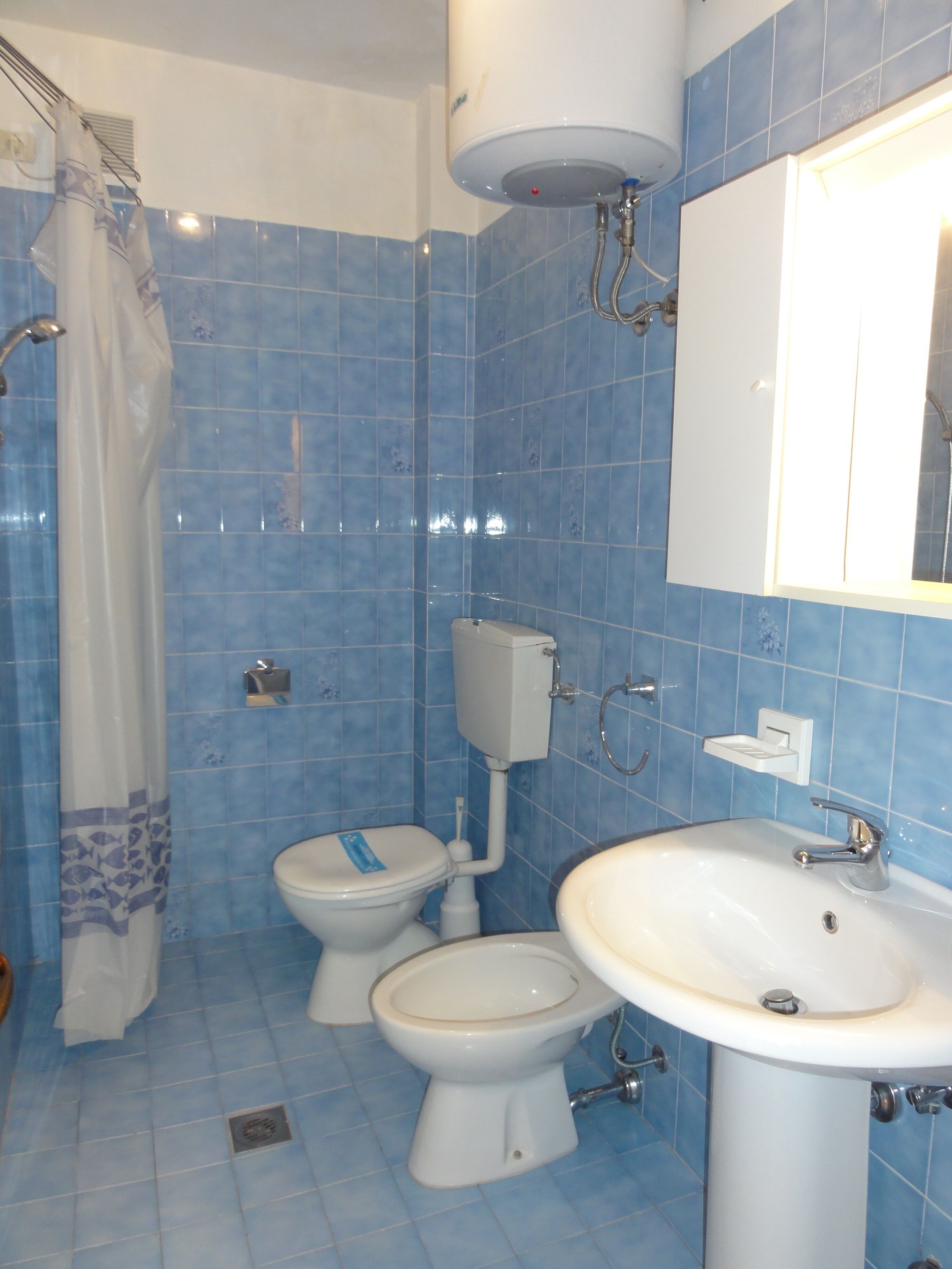 A bathroom with blue tiles, a toilet, a bidet, a sink, and a shower curtain.