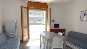 Una habitación con cama, una mesa de comedor con sillas, un sofá, un televisor y un balcón con vistas a edificios.