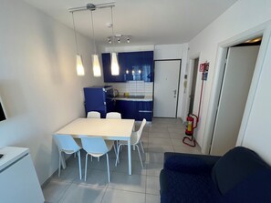 Eine kleine Küche mit Esstisch und Stühlen, einem blauen Schrank und einem Feuerlöscher.