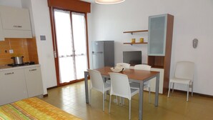 A compact kitchen with a stove, refrigerator, and a dining area with a table and chairs. - Condominio Simma 2 (San Michele al Tagliamento)