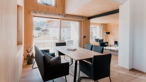 Un comedor moderno con una mesa de madera y sillas negras, ventanas amplias y vistas a una zona residencial.