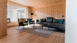 Una sala de estar moderna con paredes de madera, un ventanal grande y un sofá de cuero negro.