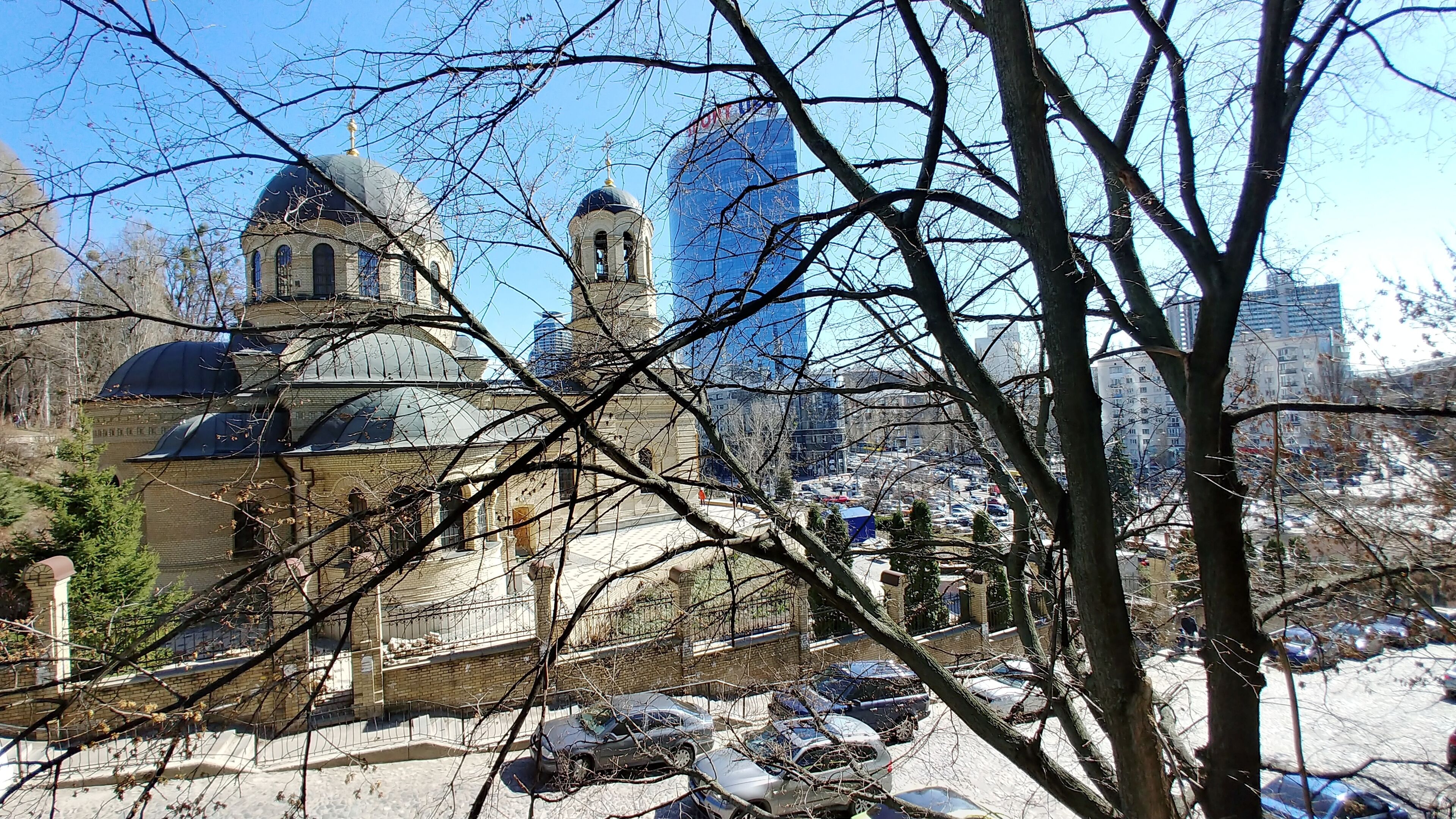A historic building with domed architecture, surrounded by modern skyscrapers and a parking area.