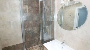 A bathroom with a glass-enclosed shower, a sink, and a mirror.