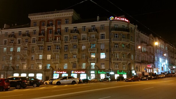 A multi-story building with ProCredit Bank signage, multiple balconies, and a street in front with parked cars. - Kiev Rent Apartments (Kyiv)