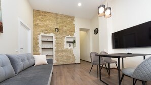 A modern living room with a grey sofa, a dining table with chairs, a TV, and a brick wall with shelves. - Kiev Rent Apartments (Kyiv)