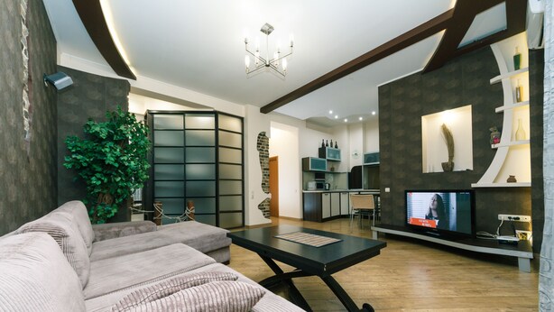 Ein modernes Wohnzimmer mit Ecksofa, einem Essbereich und einer Küche im Hintergrund.