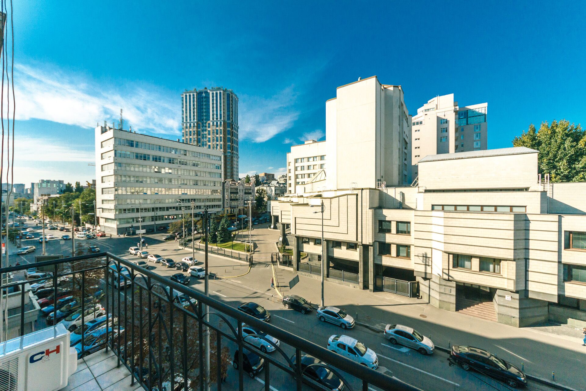 Paisagem urbana com edifícios modernos, rua movimentada e área de estacionamento.