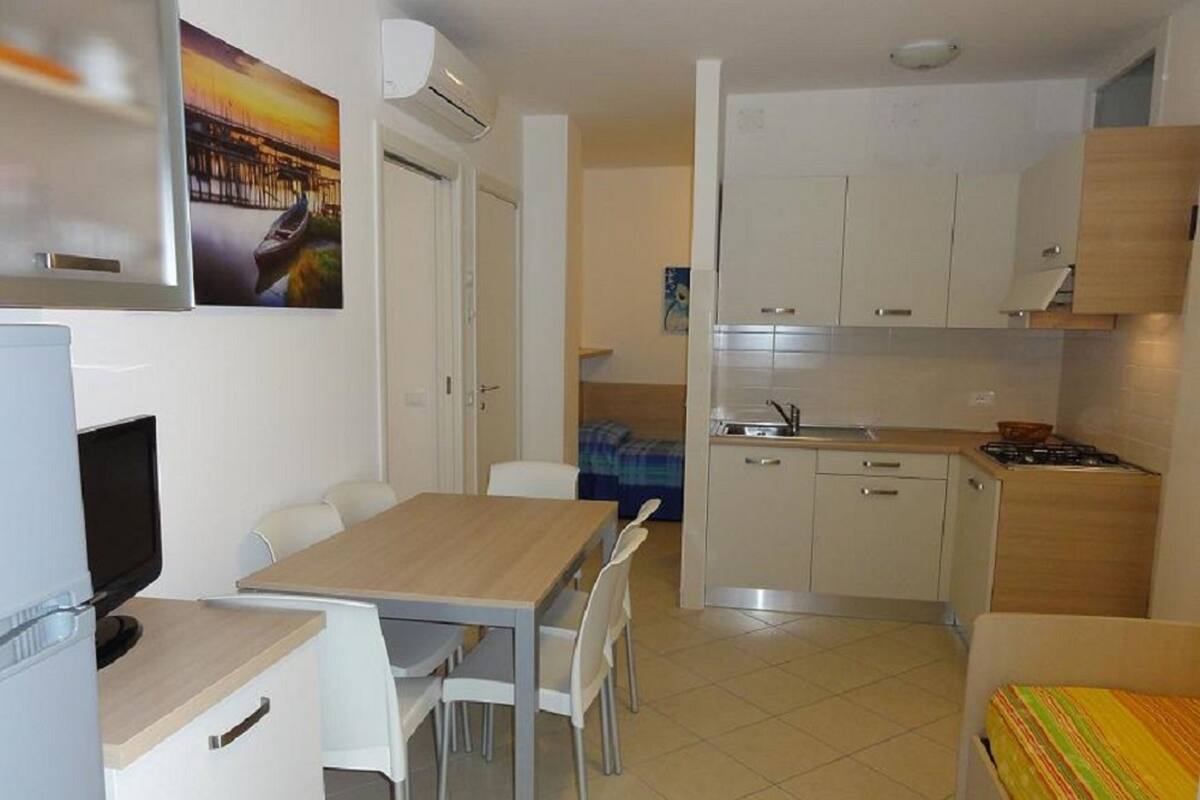 A compact kitchen with white cabinets, a dining area with a table and chairs, and a small TV.