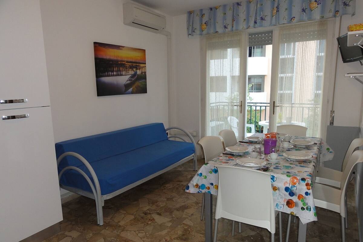 A dining area with a table set for two, a blue sofa, and a window with curtains.
