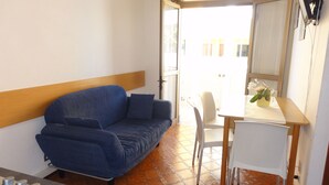 A compact room with a blue sofa, a small table, a chair, and a stove. - Condominio Stella Mattutina (San Michele al Tagliamento)