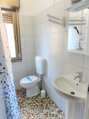 A bathroom with a toilet, bidet, sink, and a window with blinds. - Condominio Stella Mattutina (San Michele al Tagliamento)