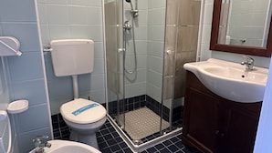A bathroom with a glass-enclosed shower, a white toilet, a bidet, and a sink with a mirror. - Condominio Storione (San Michele al Tagliamento)